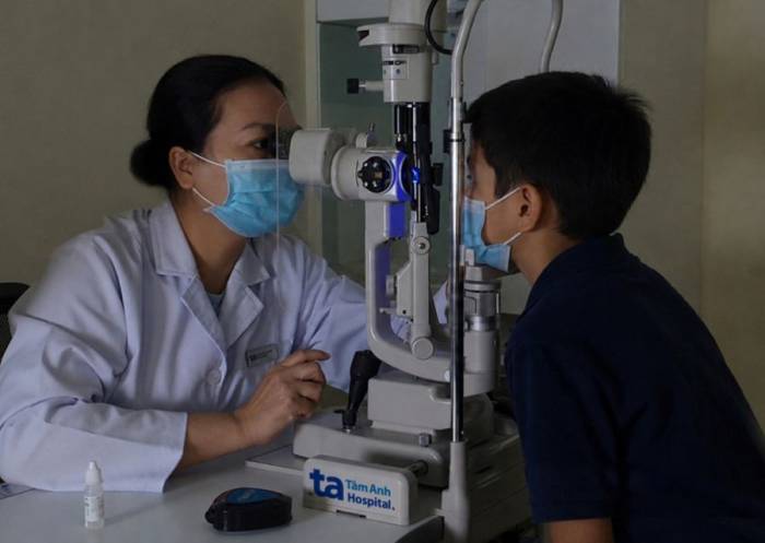 Bác sĩ Hải tắt đèn, soi ánh sáng xanh để kiểm tra bề mặt giác mạc của bé Long. Ảnh: Bệnh viện Đa khoa Tâm Anh