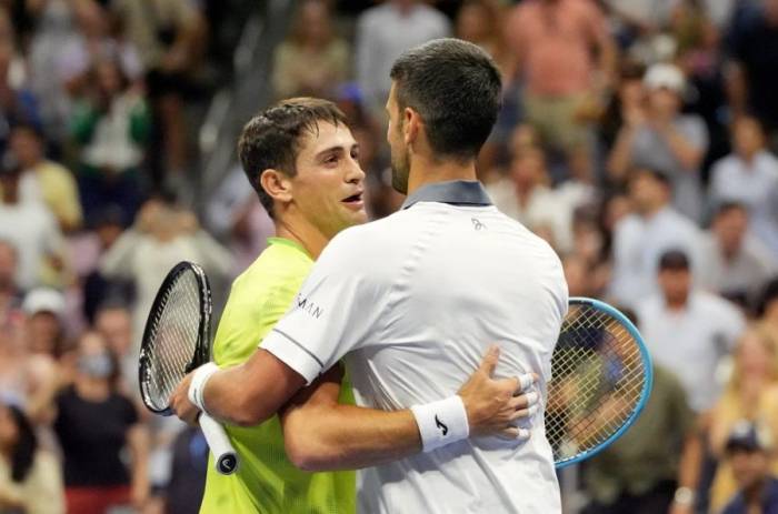 Novak Djokovic ôm Mariano Navone (trái) sau trận đấu ở vòng một Mỹ Mở rộng 2026, trên sân Arthur Ashe, New York, Mỹ ngày 30/8/2026. Ảnh: Reuters