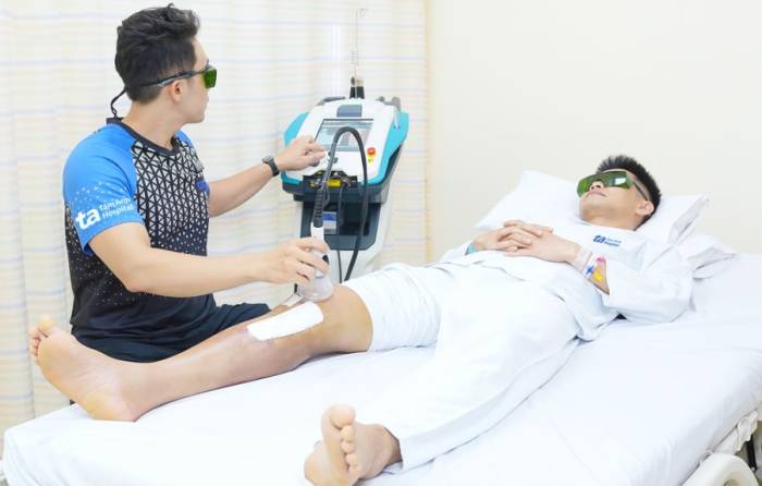 Kỹ thuật viên trị liệu laser giúp anh Đạt giảm đau, sưng nề, sớm đi lại. Ảnh: Bệnh viện Đa khoa Tâm Anh