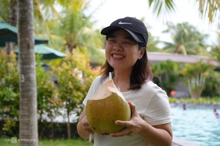 Chị Ánh Nguyệt thưởng thức nước dừa mới hái từ trên cây, bên cạnh hồ bơi. Ảnh: Phạm Linh
