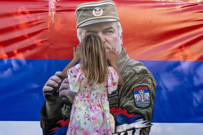 Một bé gái chạm vào lá cờ có in hình Ratko Mladic, khi người dân tập trung tại Nhà thờ St. Luke – nơi đặt thi hài của nhân vật này trước khi an táng – ở Belgrade, Serbia, ngày 7/9/2026. Ảnh: Reuters