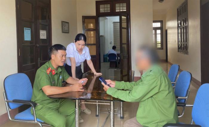 Công an xã và nhân viên ngân hàng giải thích cho người đàn ông không chuyển tiền cho đường dây lừa đảo. Ảnh: