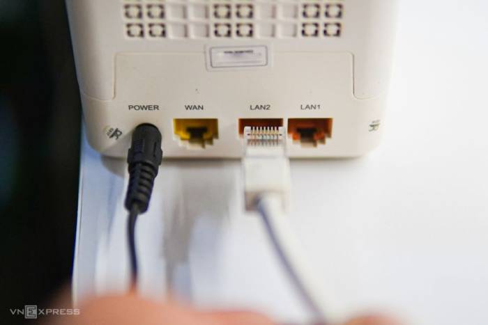 Hình ảnh cận cảnh tay người đang cắm cáp Ethernet vào cổng LAN của modem/router Wi-Fi kết nối Internet. Ảnh: Lưu Quý