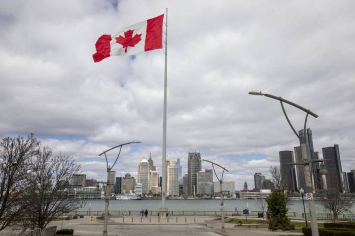 Quốc kỳ Canada ở thành phố Windsor, bang Ontario ngày 1/4. Bên kia sông là thành phố Detroit, bang Michigan, Mỹ. Ảnh: AFP