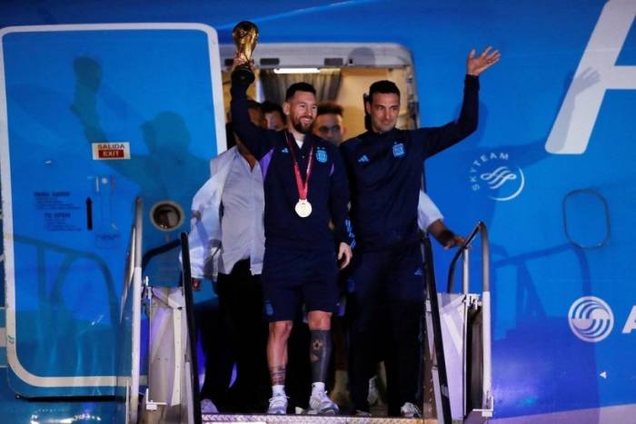 Lionnel Messi gương cao cúp vàng cùng HLV Lionel Scaloni (phải) vẫy tay chào khi đội tuyển Argentina hạ cánh xuống phi trường Ezeiza, Buenos Aires ngày 20/12/2022, sau chức vô địch World Cup 2022. Ảnh: Reuters