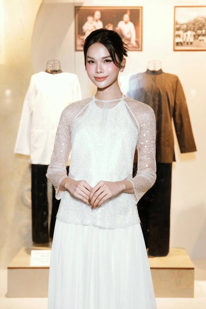 Người mẫu Tâm Như Người đẹp chọn áo bà ba cách điệu màu trắng, phần thân phủ chất liệu ánh nhũ, tay áo xuyên thấu lấp lánh, kết hợp chân váy dài xếp nếp. Cô búi tóc gọn, trang điểm tông hồng nhẹ nhàng, tôn nét thanh tú.