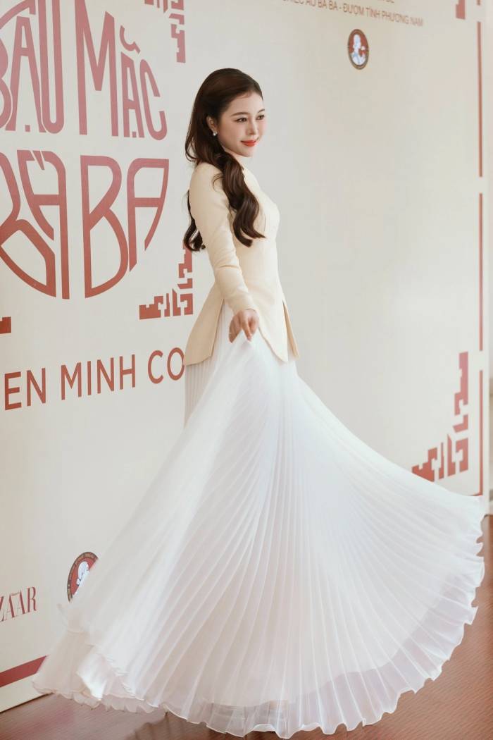 Hoa hậu Kiều Duy tạo dáng với bà ba cách điệu màu kem, dáng ôm eo, phối chân váy xếp ly dài chấm đất.