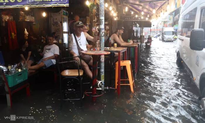 Du khách nước ngoài kê cao ghế, uống bia giữa nước ngập trên đường Bùi Viện, ngày 23/9. Ảnh: Quỳnh Trần